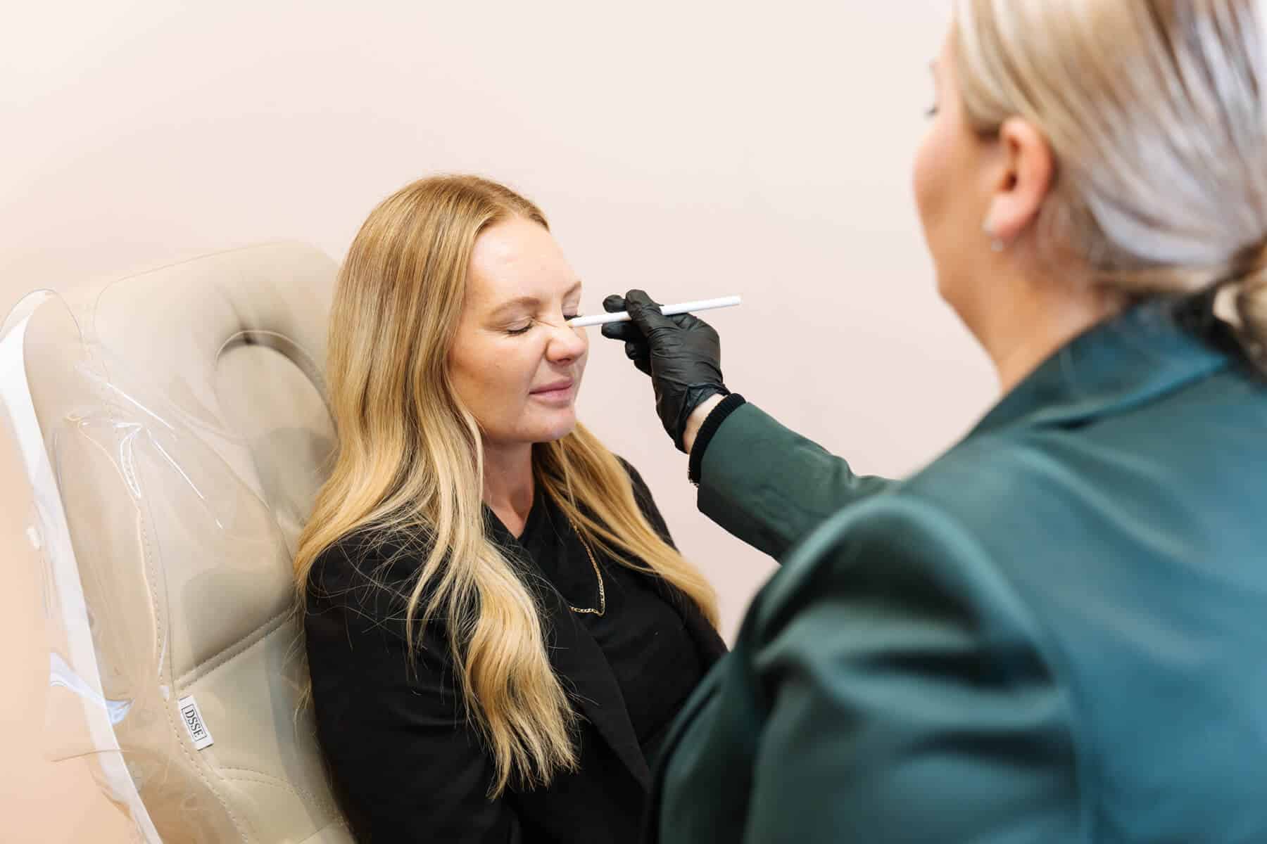 Patient scrunching their nose for bunny lines treatment at Sydney cosmetic clinic, while cosmetic practitioner marks their scrunch lines with white pencil
