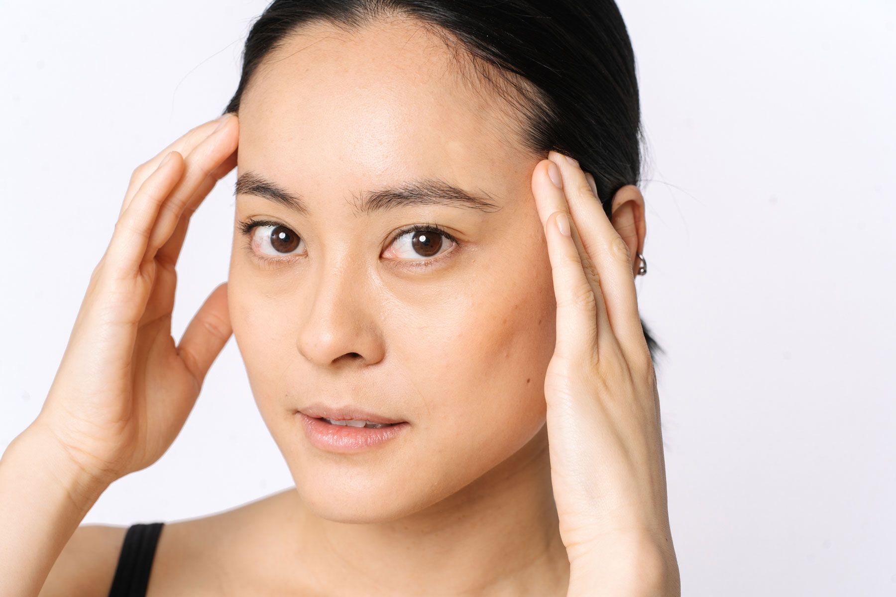 Asian female with clear skin who is using her hand to point to her upper face